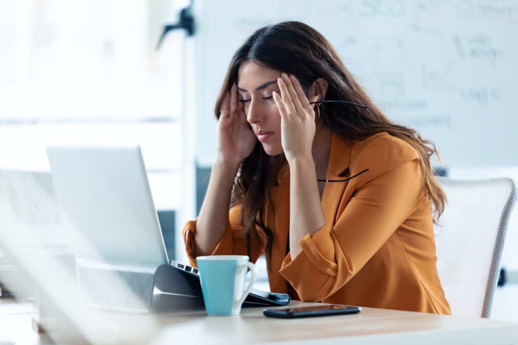 Business junge Frau mit Kopfschmerzen arbeiten mit Laptop im Büro.