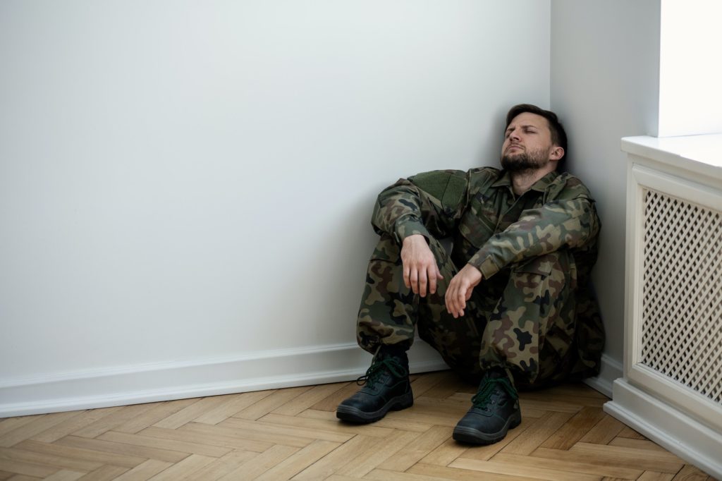 Deprimiert Armee Mann in Uniform sitzt in einer Ecke eines leeren ro