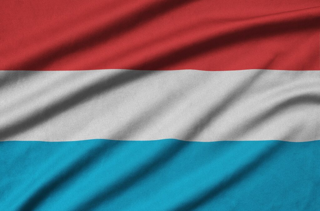 Die luxemburgische Flagge ist auf einem Sportstoff mit vielen Falten abgebildet. Sportmannschaft winkt mit Fahne