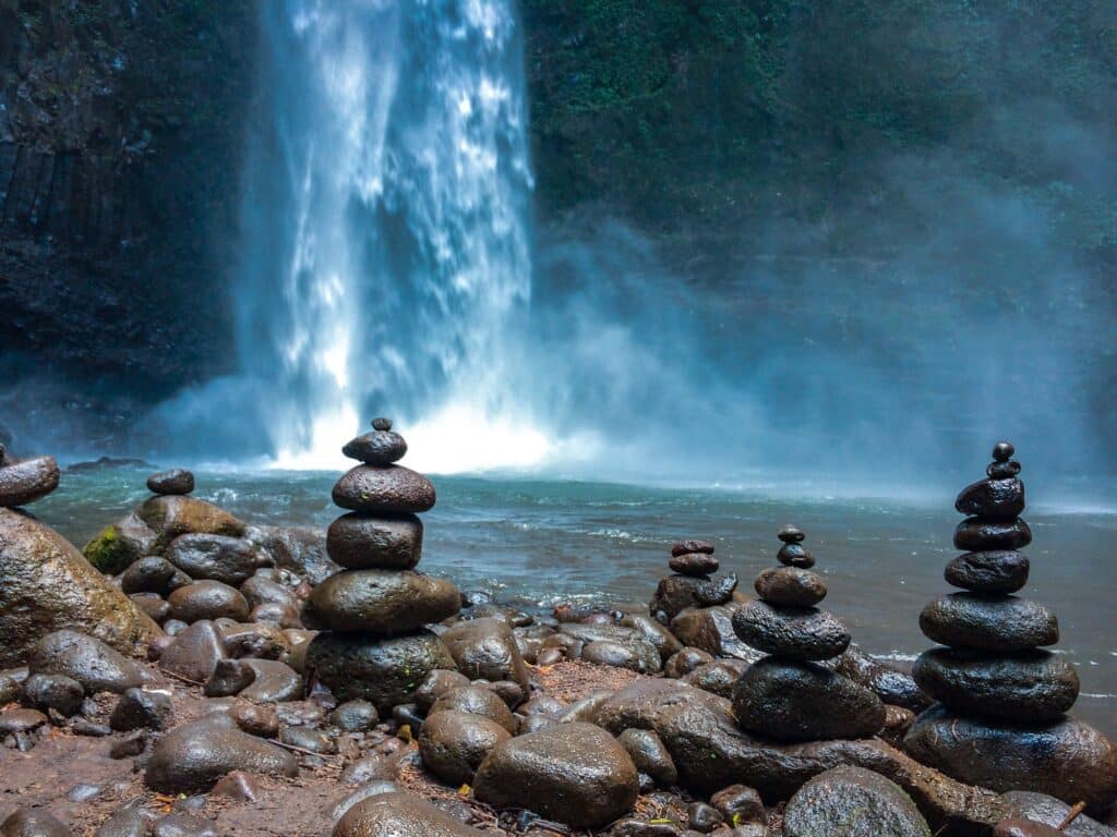Gestapelte Steine zur Meditation vor einem blauen Wasserfall im Dschungel
