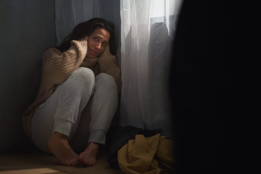 Verängstigte Frau sitzt auf dem Boden und bedeckt ihren Kopf aus Angst vor häuslicher Gewalt