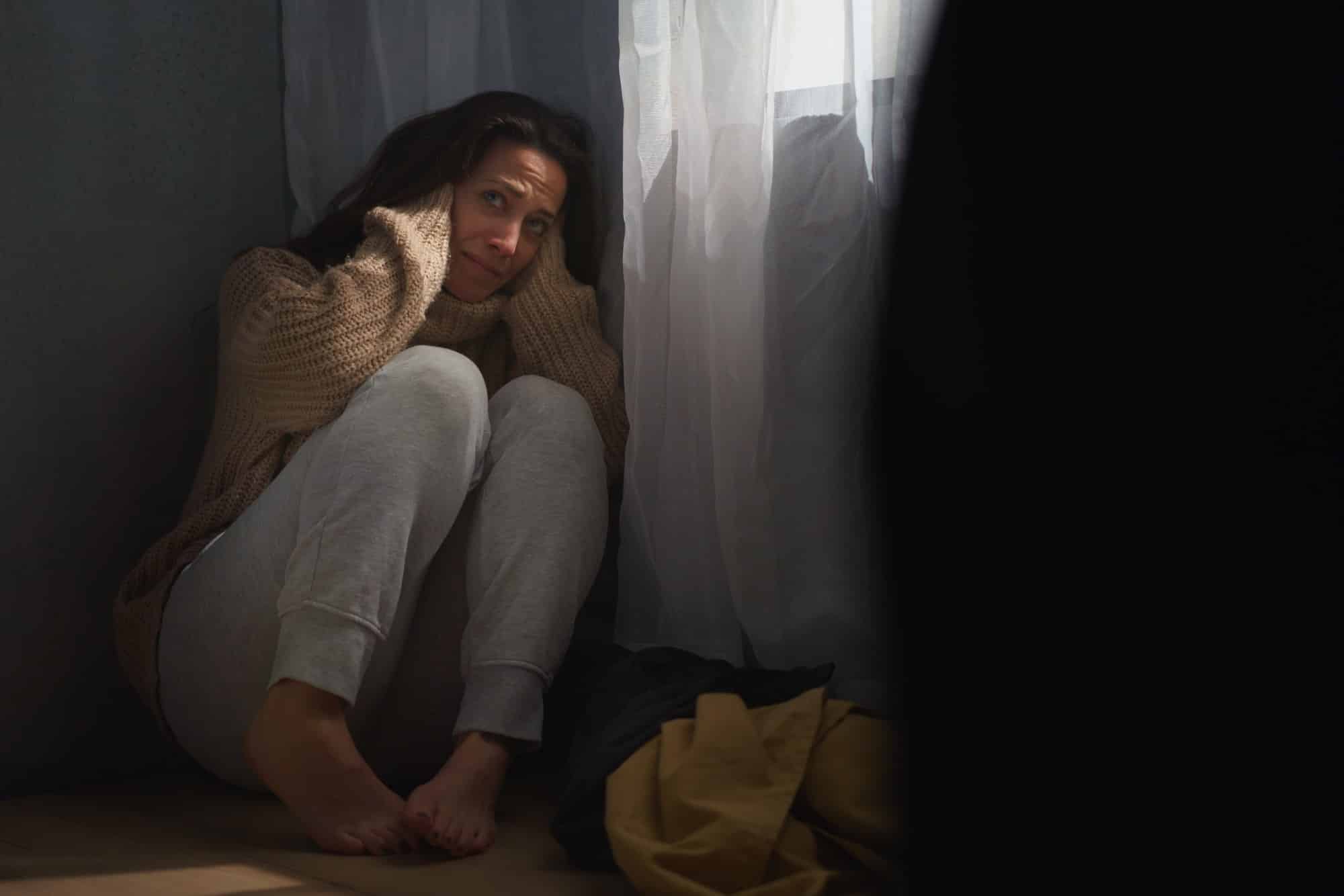 Verängstigte Frau sitzt auf dem Boden und bedeckt ihren Kopf aus Angst vor häuslicher Gewalt