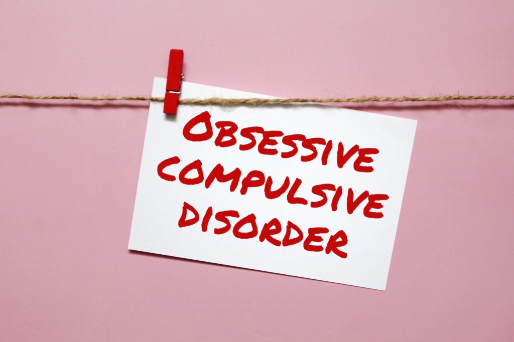 Aufkleber mit der Aufschrift obsessive compulsive disorder hängen an einem Seil auf einem rosa Hintergrund