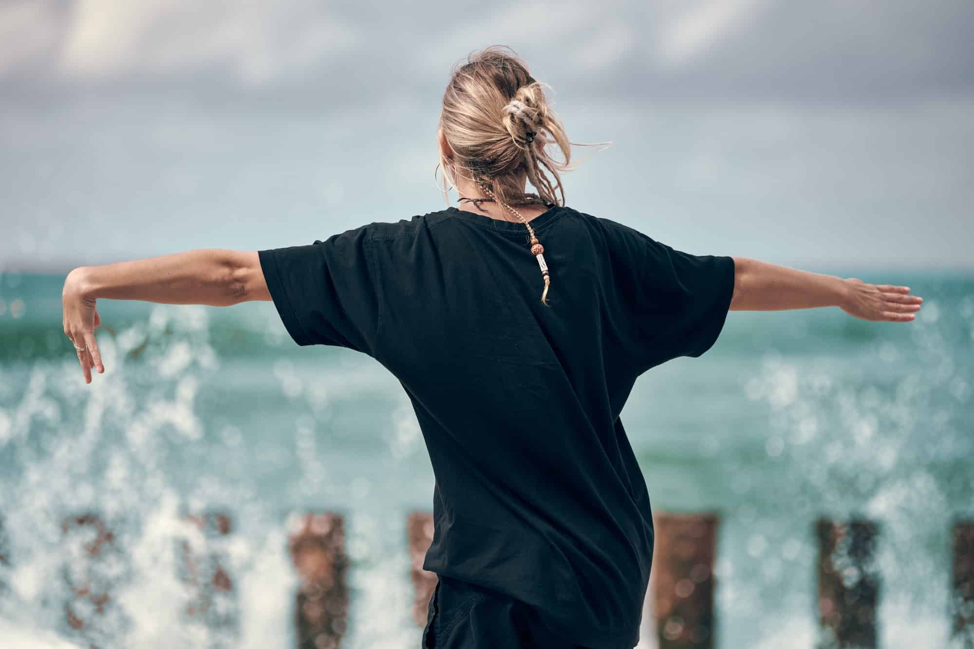 Frau tanzt zu Musik an der Meeresküste, Rückansicht, Tänzer bei Kunstperformance-Musikfestival im Freien